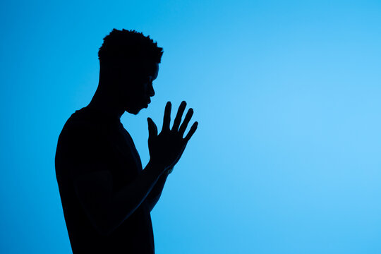 Anonymous black man praying with clasped hands on blue background
