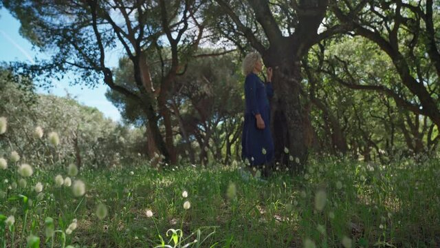 A European woman, middle-aged in a dress, walks on a prak with tall grass. With a philosophical romantic mood. Slow motion