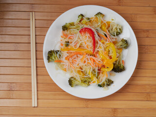 Glass noodle salad with vegetables and pepper on a wooden table.