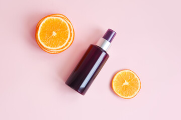 Unbranded brown cosmetic spray bottle and orange slices on pink background. Natural organic spa cosmetics, Spray concept. Body mist, brume corps. Percent sign concept. Mockup, template.