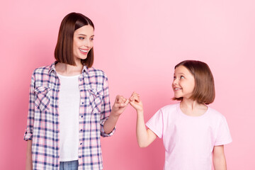 Portrait of attractive cheerful sisters holding fingers affection care support isolated over pink pastel color background