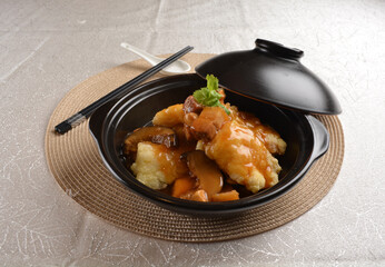 deep fried grouper fish fillet seafood in black hot clay pot with vegetables and mushroom in dark soy sauce white background premium asian halal menu