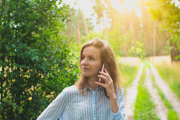 Fototapeta premium Beautiful girl with fair hair is talking on phone in forest. Young woman lost on the nature. No signal phone connection.