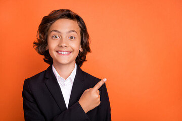 Photo of happy positive cheerful little boy point finger empty space good mood news isolated on orange color background