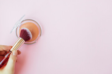 lady's hand holding make up brush dipping into peach brown face powder