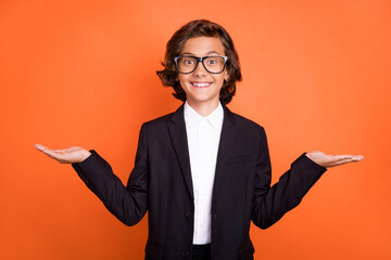Photo of brunette excited little boy hold hands scales empty space wear suit formalwear isolated on orange color background