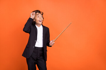 Photo of young amazed shocked happy boy look empty space point stick isolated on orange color...