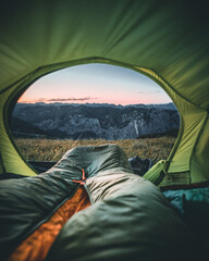 person sitting in the tent with cup looking at the mountain landscape. View from inside