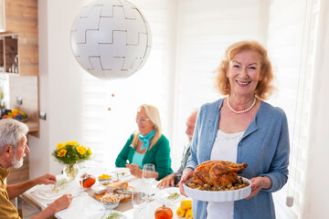 Senior woman serving roasted chicken for Thanksgiving dinner with friends