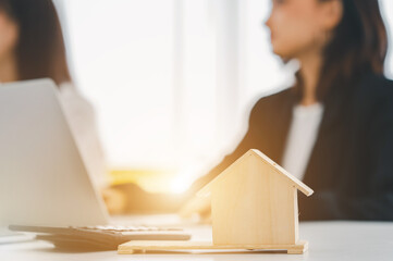businessman analyzing data on laptop with a business woman using a calculator at the office. Model houses and banknotes.