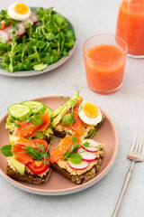 Healthy tasty breakfast, sandwiches with avocado and salmon, cucumbers and tomatoes, radishes and microgreens of peas with boiled egg and root salad, grapefruit smoothie in a glass