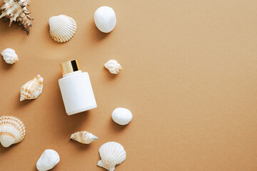 Suntan cream lotion bottle and seashells on sandy color background. Flat lay, top view, overhead.