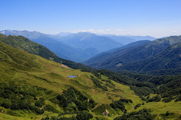 small mountain lake on the alpine meadows and valley covered with forest in caucasus