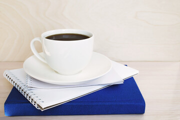 A white cup of coffee sits on a stack of notebooks.