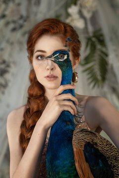 Conceptual portrait of a red-haired woman with a blue peacock