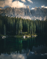 The Latemar mt and a wood reflected in the lake Karersee in a cloudy day at sunset, Dolomites, Italy