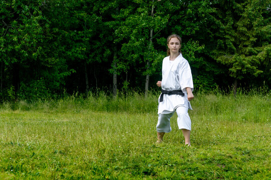 teenage girl training karate kata outdoors, performs gedan-barai (downward block)