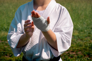 Obraz premium teenage girl in a kimono wrapping a wrist wrap around her hand before taking karate outdoors
