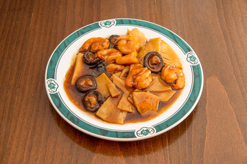Chinese restaurant recipe with chopped bamboo, stewed peeled prawns and Chinese mushrooms with soy sauce on wooden table