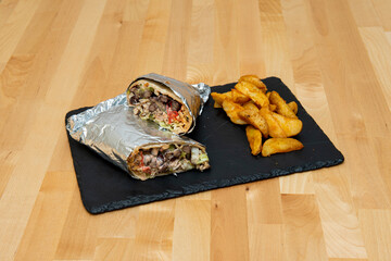 Mexican stuffed burrito with potato wedge garnish wrapped with aluminum foil on pine wood table