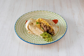 Wheat tortilla burrito stuffed with chipotle chicken, guacamole and rice with sauces on decorated plate
