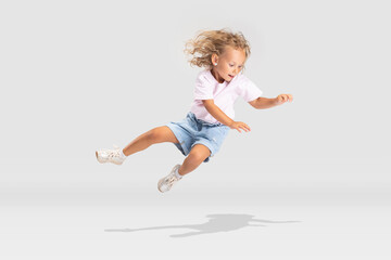 Studio shot of little preschool Caucasian girl in casual clothes falling down isolated over white studio background.