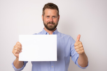 Portrait of happy smiling young business man showing blank signboard with thumb up over white background.