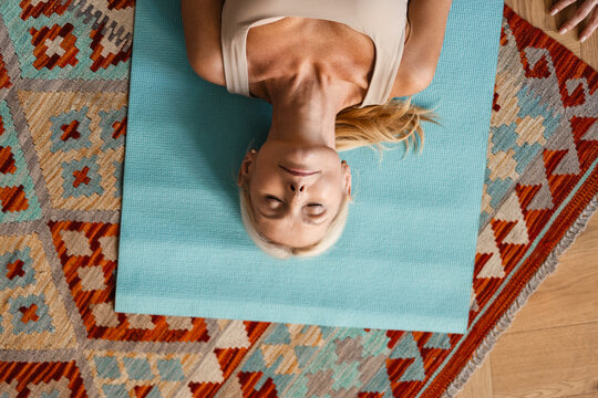 Blonde Mature Woman Lying On Mat During Yoga Practice At Home