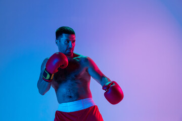 One man, professional boxer in sportwear boxing on studio background in gradient neon light....