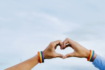 Closeup shot of a gay couple holding hands with a rainbow wristband made hands forming a heart...