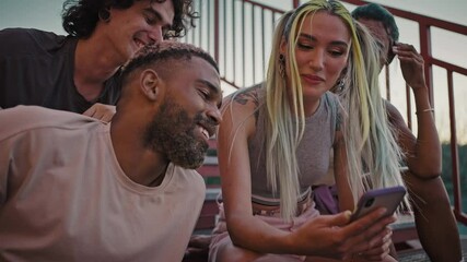 Group of young happy diverse friends spending time together, watching social media on smartphone and laughing, zoom in - Powered by Adobe