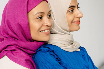 Two middle eastern women in headscarf hugging and smiling on camera