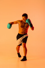 Fototapeta na wymiar Portrait of Caucasian man, professional boxer in sportwear in action and motion on studio background in yellow neon light. Concept of sport, activity, movement, wellbeing.