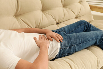Man suffering from pain in lower right abdomen on sofa at home, closeup. Acute appendicitis