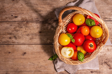 Ripe assorted tomatoes with fresh basil in a wicker basket