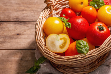 Ripe assorted tomatoes with fresh basil in a wicker basket