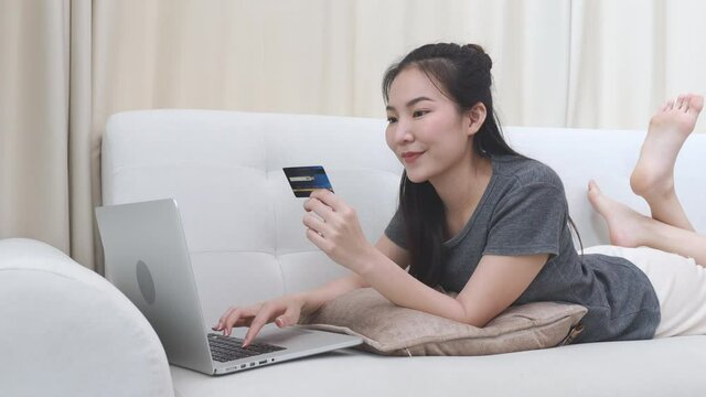 Asian woman sitting on sofa, Using laptop to shop online with credit card to register for payment ,Online transactions.