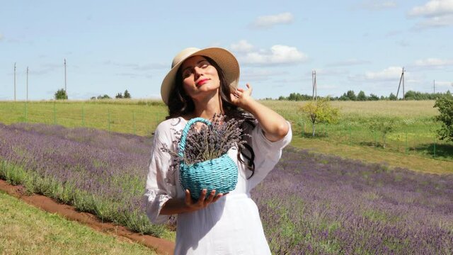 Close up of beautiful smiling woman in hat with basket of lavender.  Selective focus of girl with long hair enjoying scent of aromatic flowers. Lavender field on background. Copy space