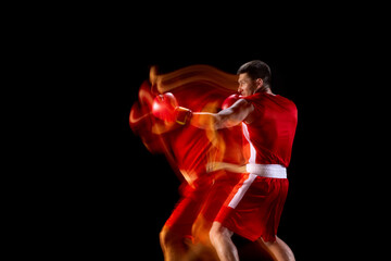 One professional male boxer in action, motion on black background in mixed lights