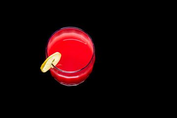 Watermelon juice, a tropical summer drink garnished  with lime and ice cubes. Top view of the glass placed on a black surface.