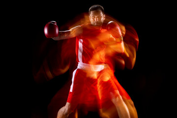 Portrait of professional male boxer in motion, action on black studio background in mixed lights....