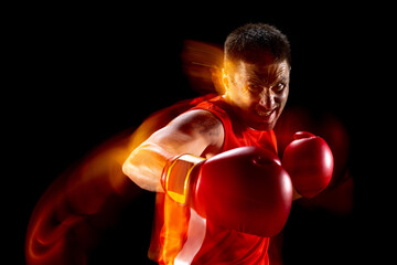Half-length portrait of one professional male boxer in motion, action on black studio background in...