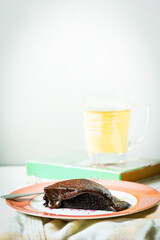 Delicious slice of moist chocolate cake on a plate with cup of tea in background.