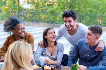 multiethnic group of university students having breakfast at the cafeteria, young friends smiling and laughing while drinking coffee and eating muffins