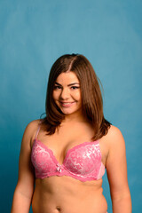 Fototapeta premium Pretty caucasian woman with plus size body wearing pink lace underwear on blue studio background