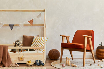 Stylish composition of cozy scandinavian child's room interior with wooden bed, red armchair, plush and wooden toys and textile decorations. Creative wall, carpet on the floor. Copy space. Template.