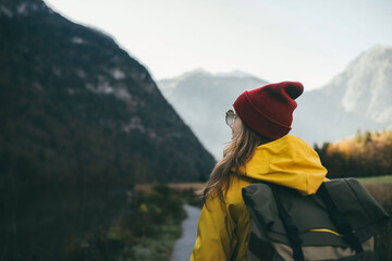 girl in a yellow jacket with a backpack in a red hat and glasses stands with her back and