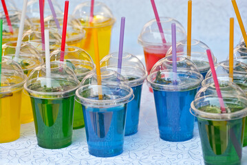 Multicolored fruit drinks close-up. Non-alcoholic drinks in plastic cups at the festival. Cocktails with juice and greens.