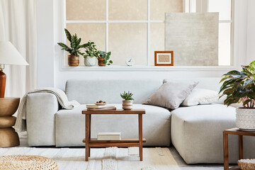 Creative composition of stylish and cozy living room with mock up poster frame, grey sofa, wooden coffee table, plants and personal accessories. Beige neutral colors. Template.