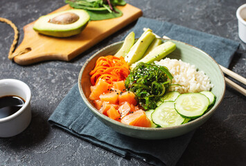 Salmon poke with avocado, seaweed, pickled carrots and cucumber on stone table.